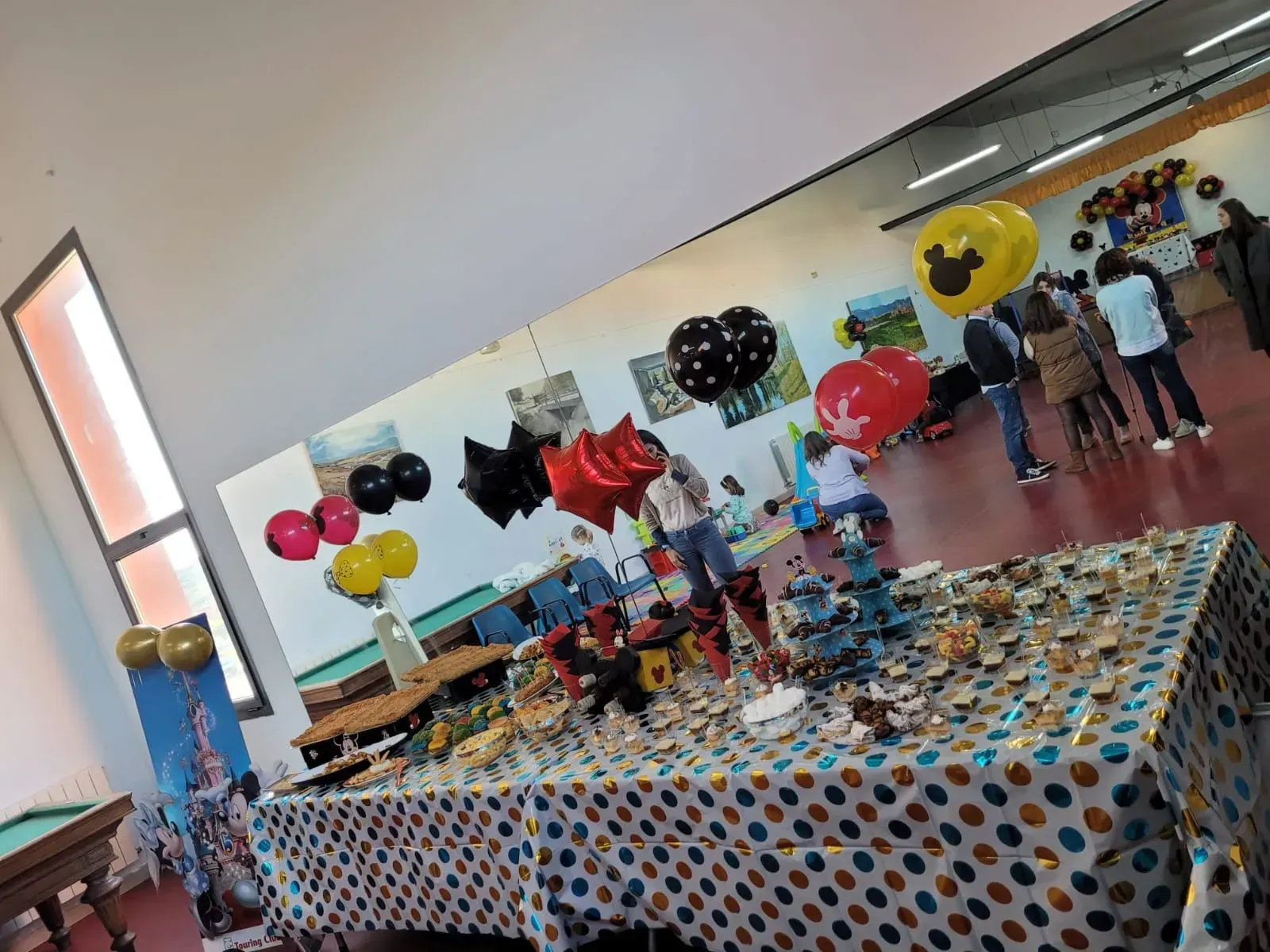Fiesta con decoraciones, globos, comida y gente con temática de Disney en una sala bien iluminada.