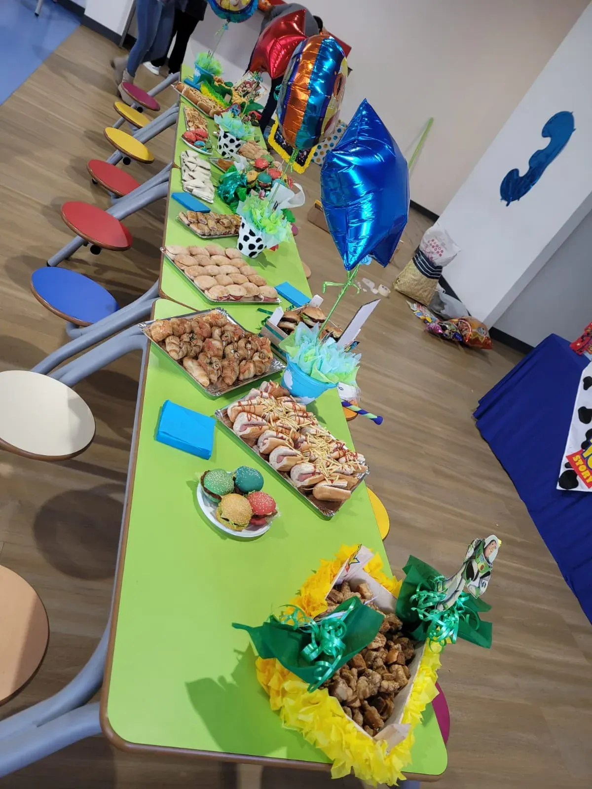 Mesa larga con bocadillos y globos; ambiente de fiesta colorido.