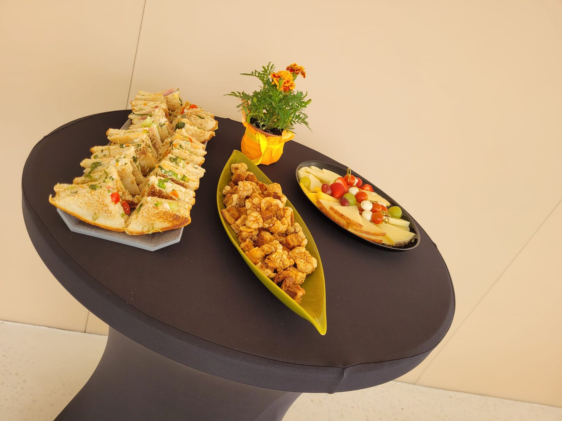 Mesa pequeña con aperitivos: bocadillos, frituras, fruta y una pequeña planta en maceta.