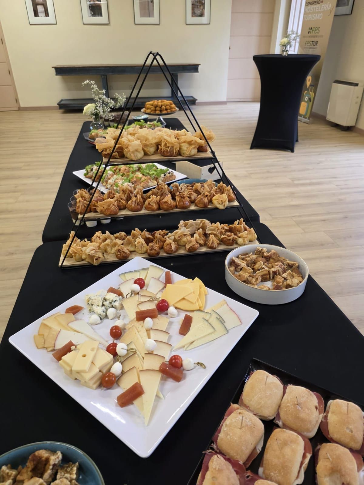 Mesa de buffet con quesos, sándwiches, aperitivos y presentación de alimentos escalonados.