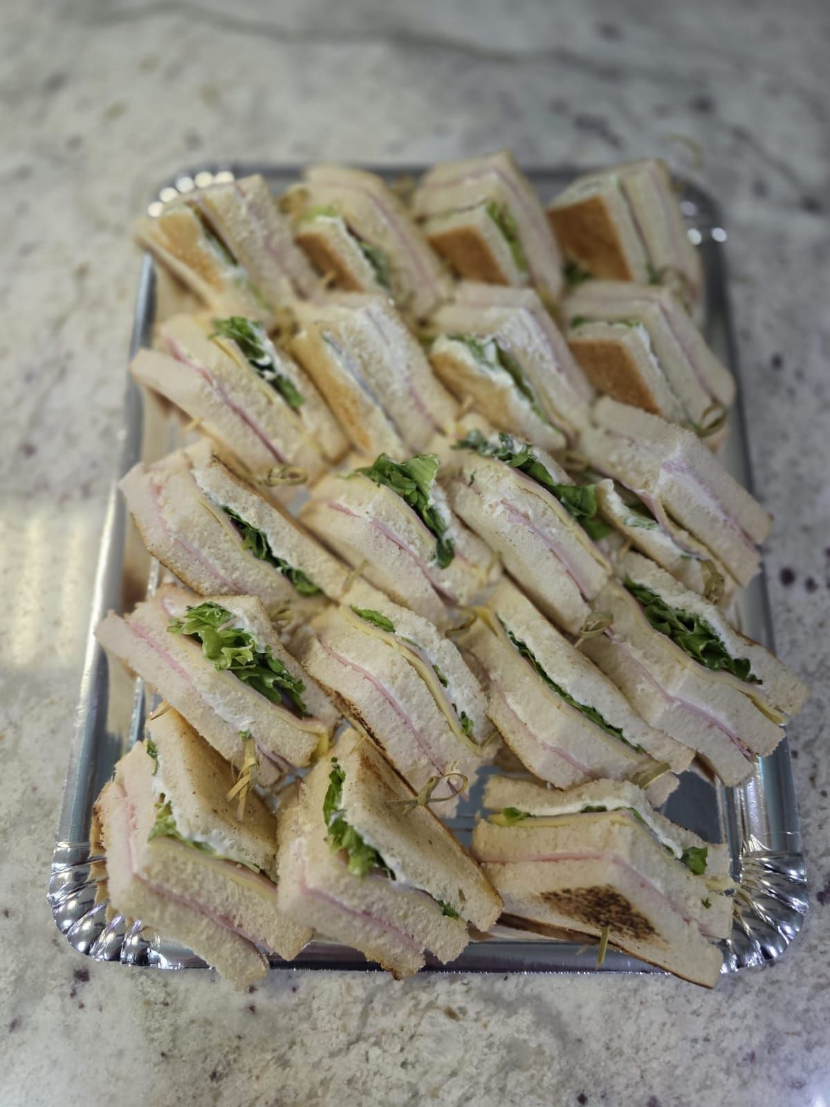Sándwiches dispuestos en una bandeja de plata, con pan blanco con rellenos visibles.