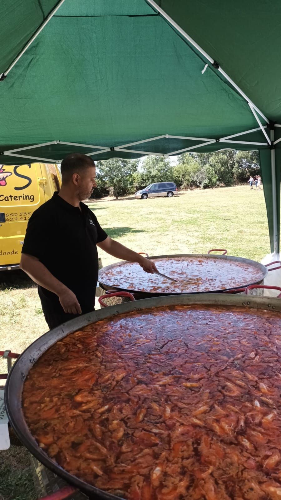 Hombre revolviendo una paella gigante en una sartén grande al aire libre, bajo una carpa.