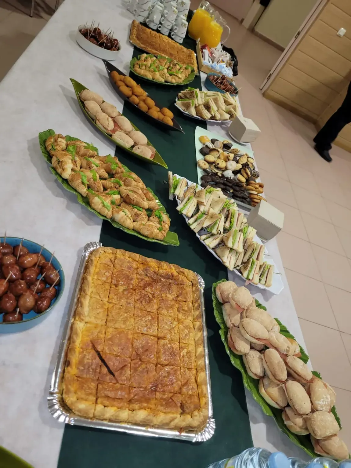Una mesa repleta de pasteles y aperitivos variados, incluidos sándwiches y dulces, preparada para una reunión.