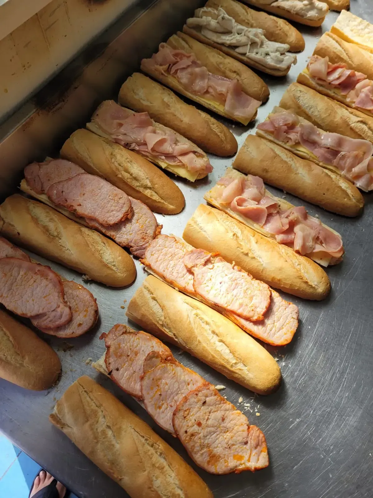 Baguettes cortadas por la mitad, rellenas de distintas carnes, dispuestas sobre una superficie metálica.