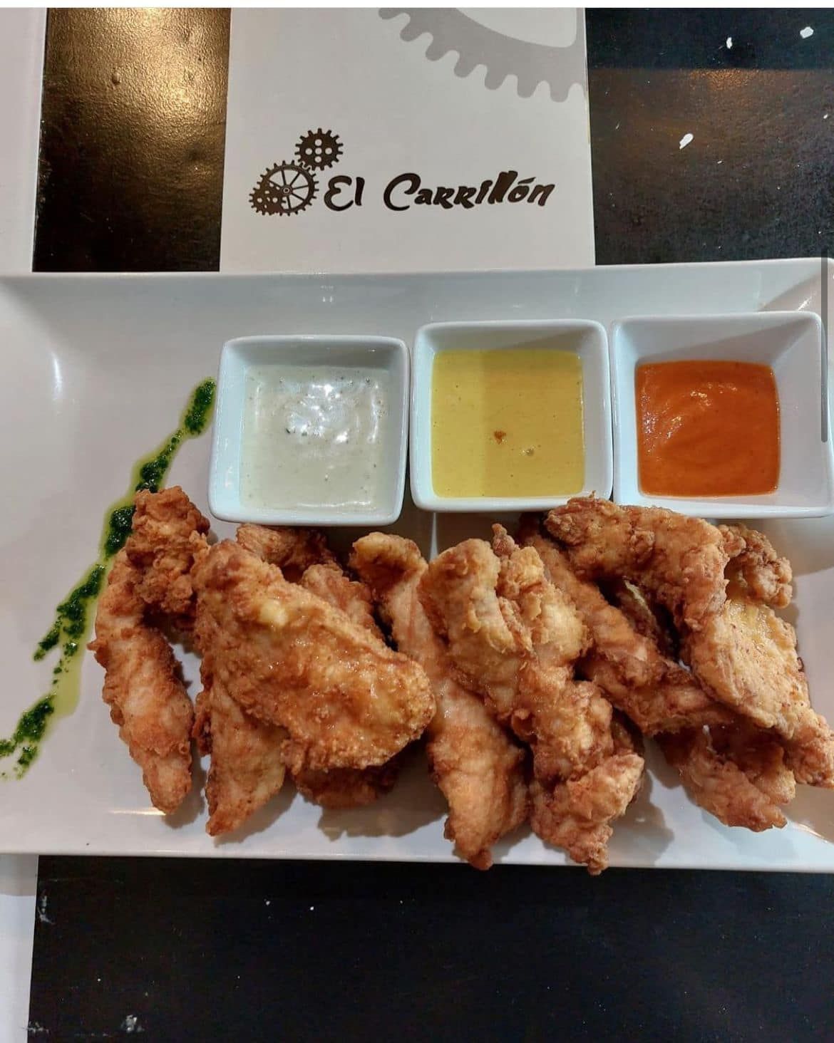 Un plato blanco con pollo frito y salsas para mojar.