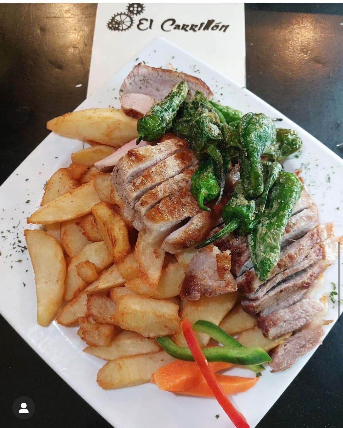 Un plato blanco cubierto con carne y papas fritas.
