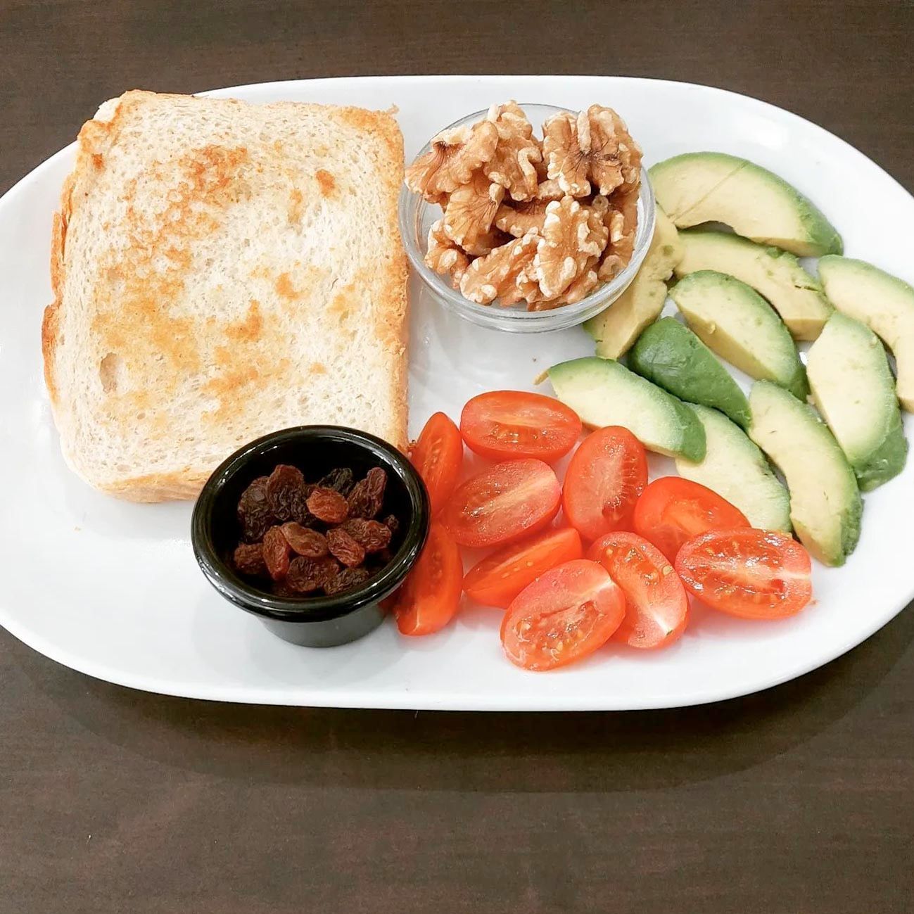Un plato blanco cubierto con tostadas de aguacate, tomates y nueces.