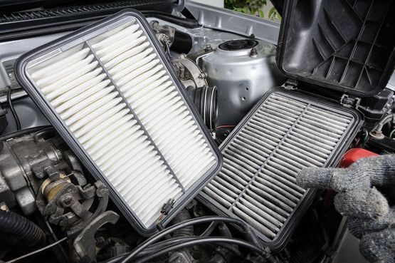 Una persona señala un filtro de aire sucio en el motor de un automóvil.