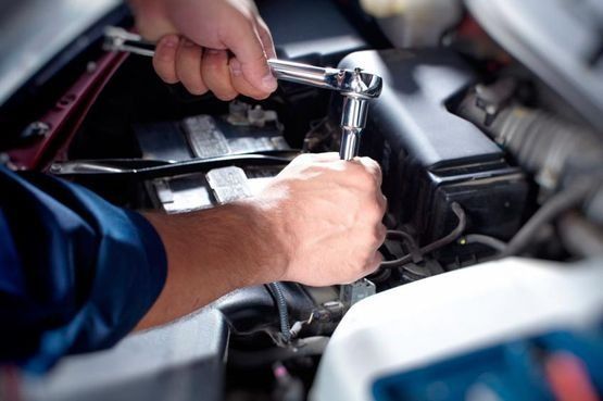 Un hombre está trabajando en el motor de un automóvil con una llave inglesa.