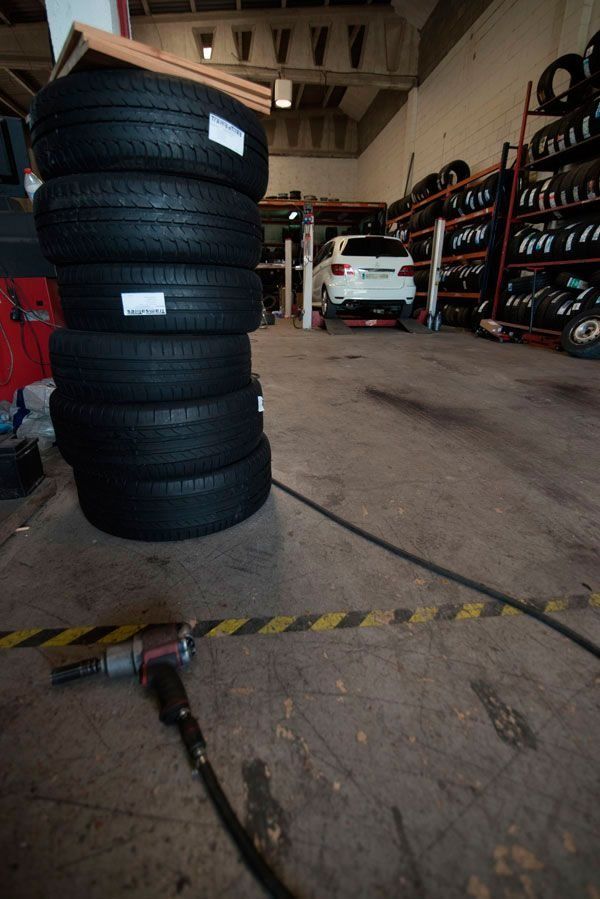 Una pila de neumáticos en un garaje con un coche al fondo.