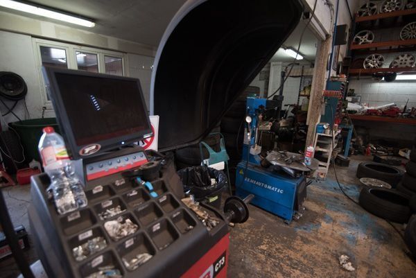 Un monitor de computadora está colocado encima de una balanceadora de ruedas en un garaje.