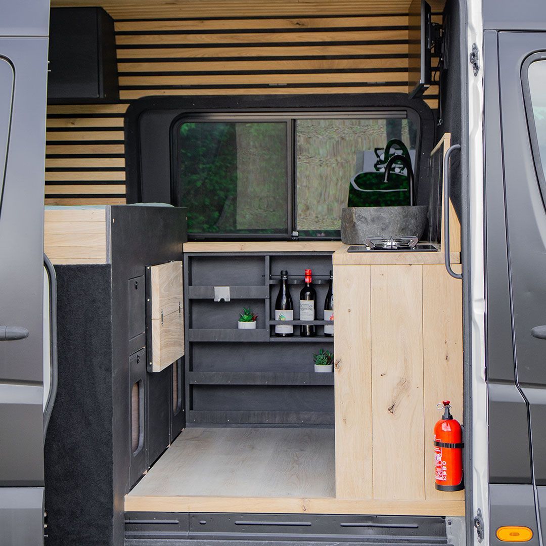 Interieur van een camper met houten accenten, een kleine keuken, een raam en een brandblusser.