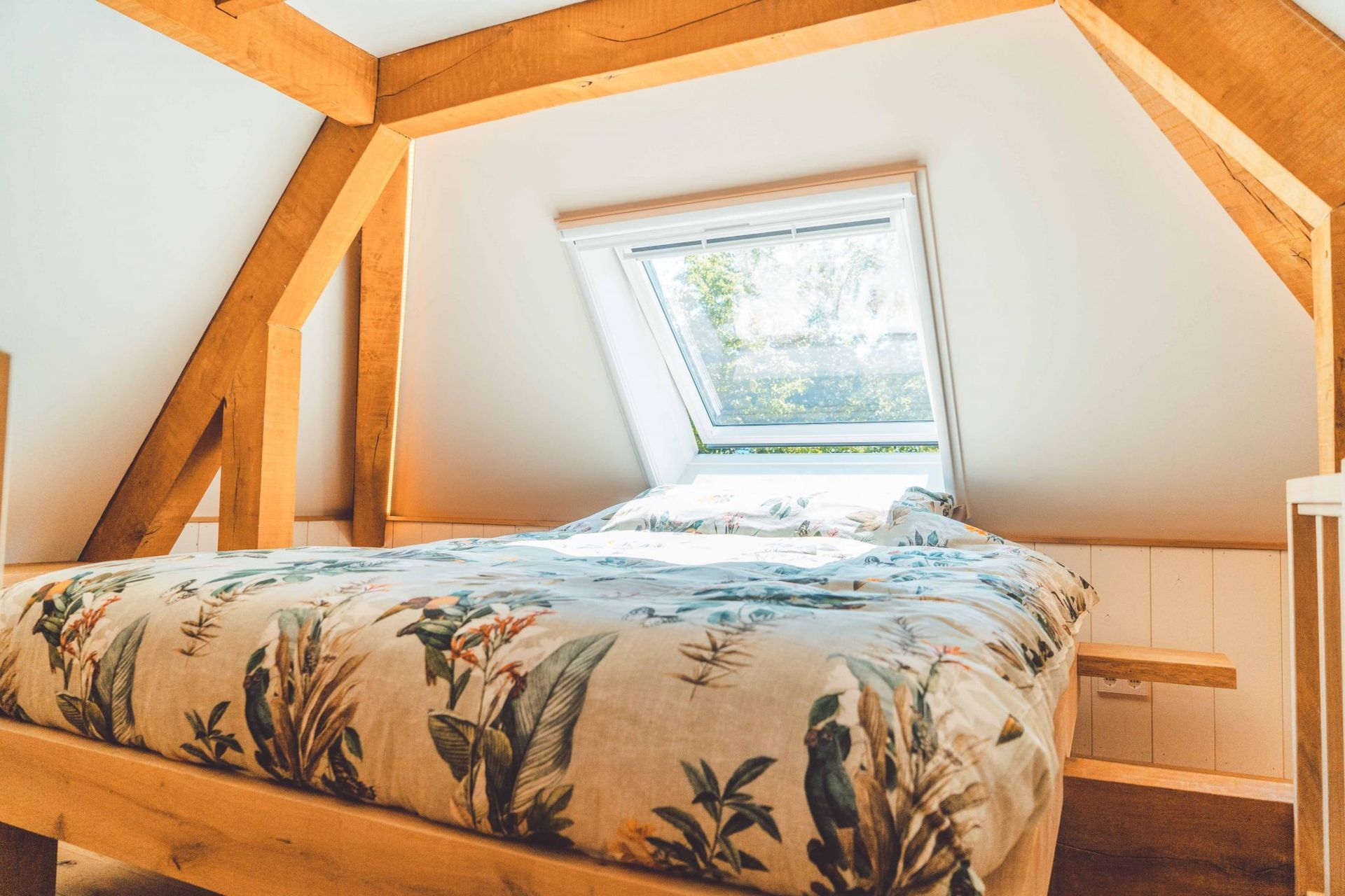 Slaapkamer met houten balken, een bed met bloemenbeddengoed en een dakraam.