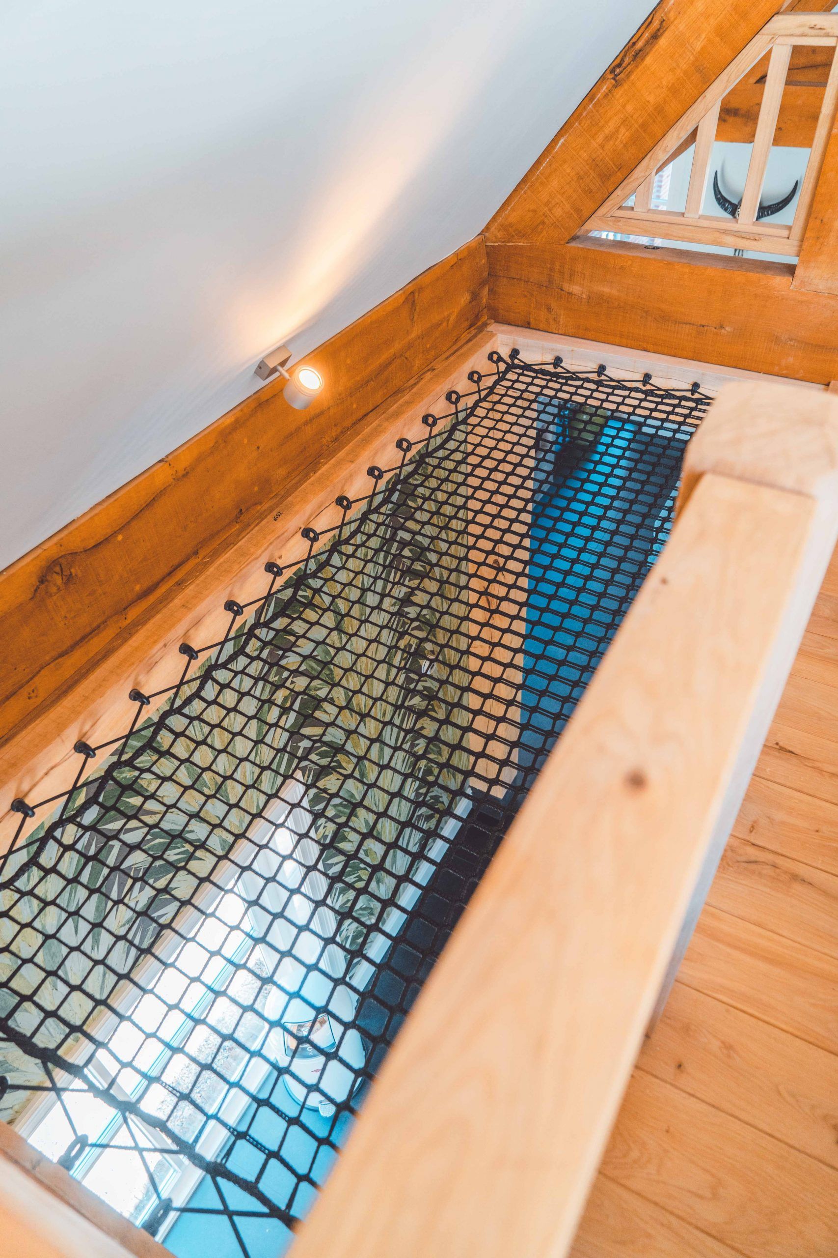 Loft met zwarte veiligheidsnetvloer, houten balken en sierlijsten. Daglicht door de vloer.