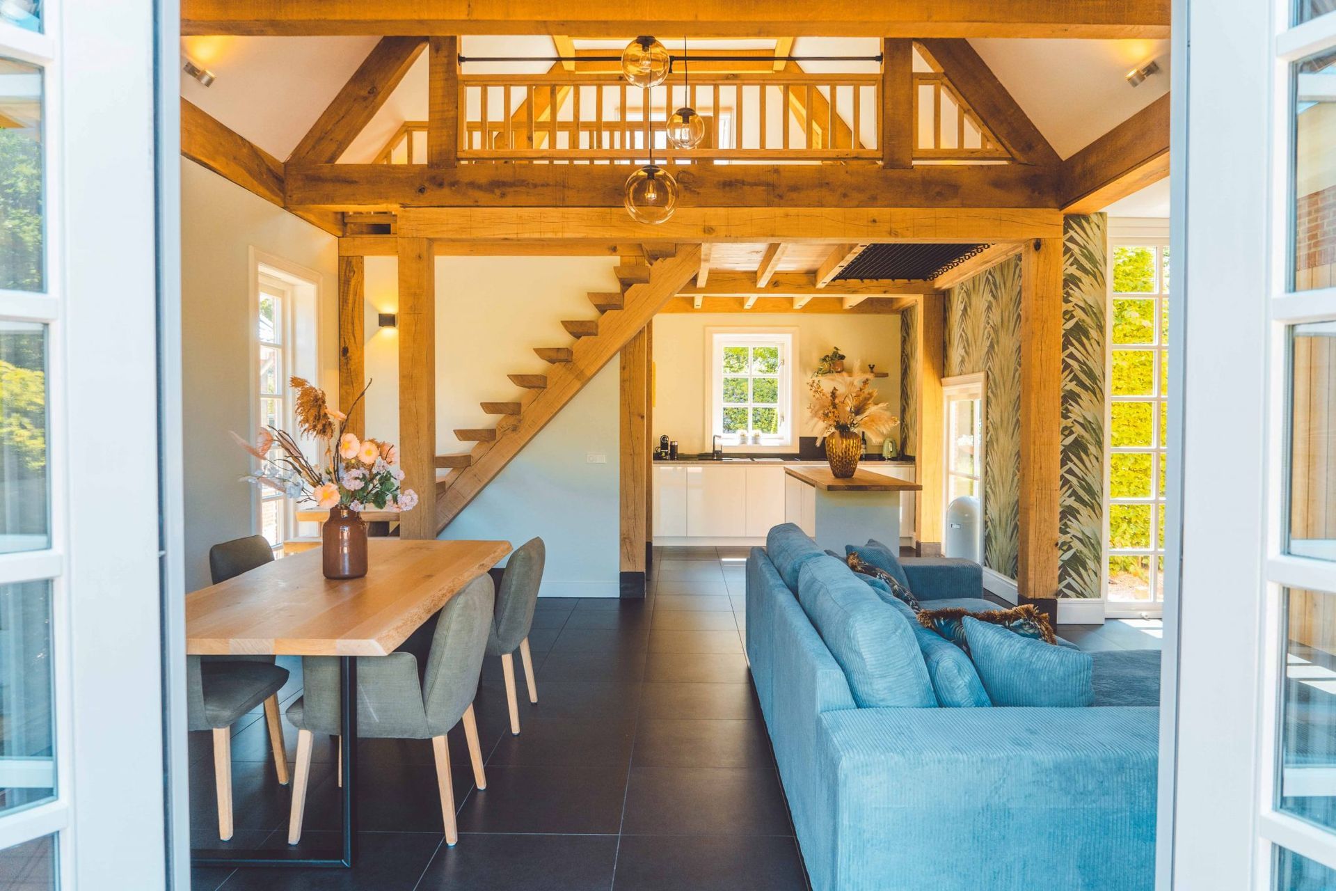 Modern interieur met houten balken, eettafel en blauwe bank, gezien vanuit een deuropening.