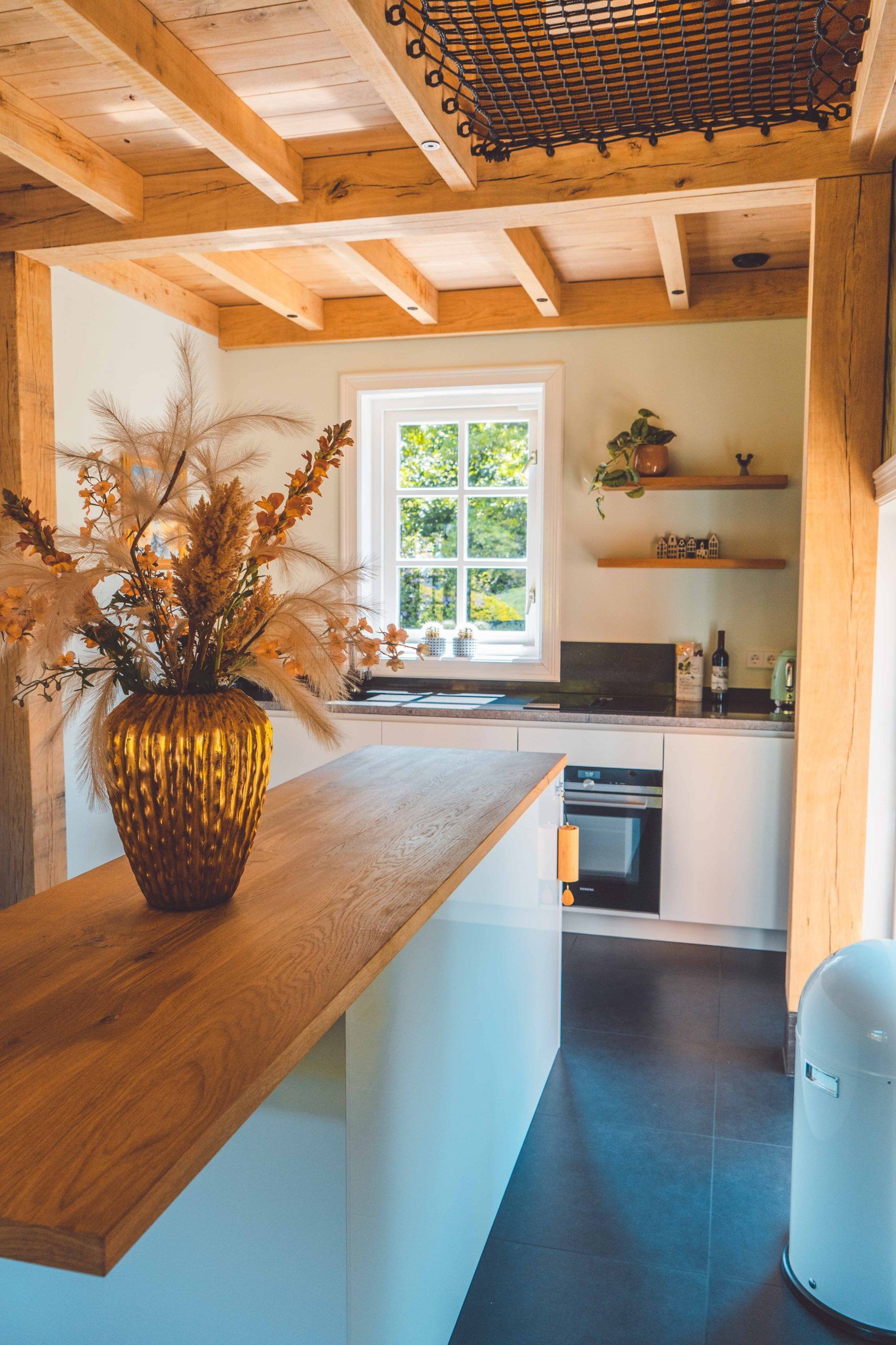 Keuken met houten balken, witte kasten en een vaas met gedroogde bloemen op het aanrecht.