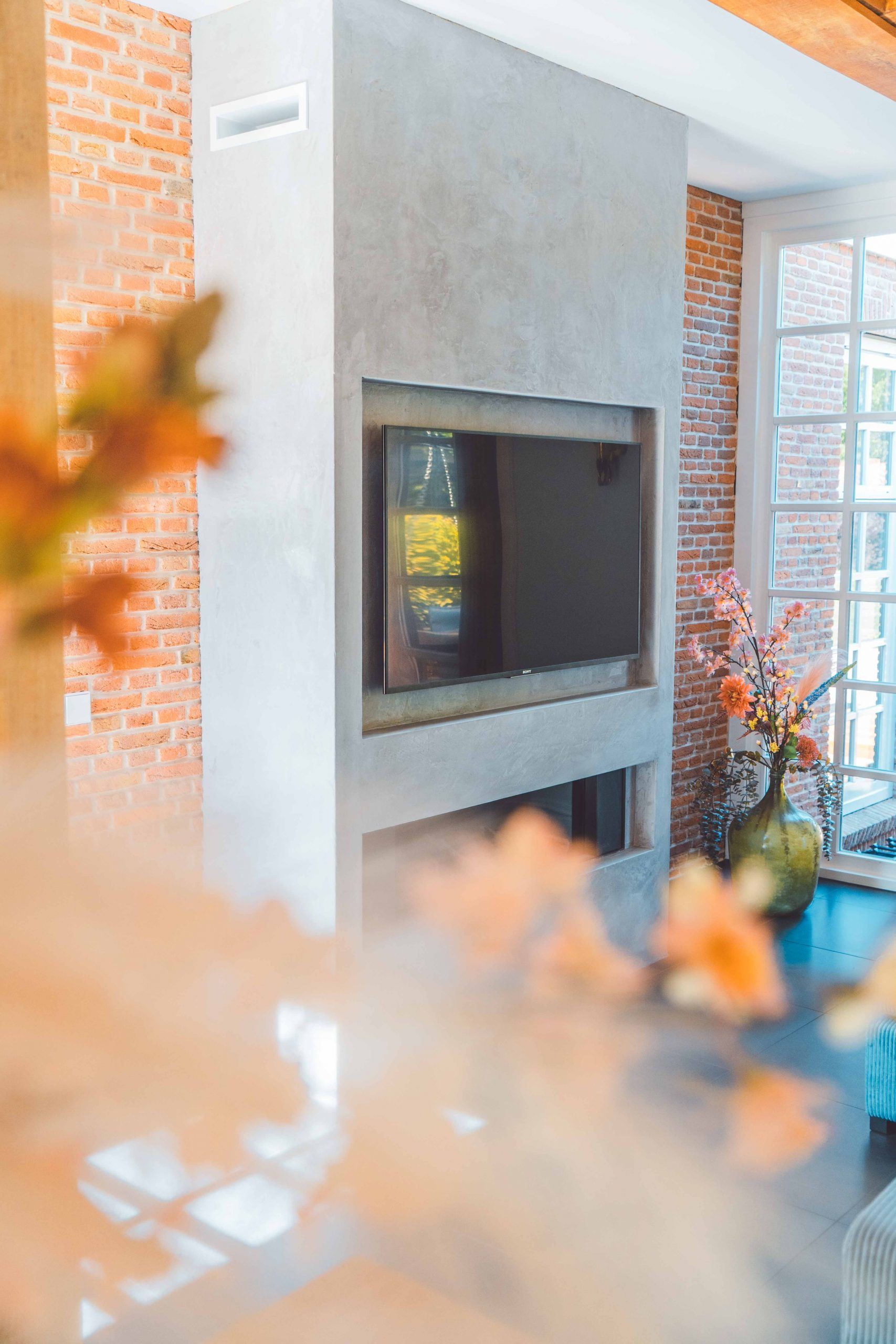 Moderne open haard met ingebouwde tv, bakstenen muur en decoratieve bloemen.