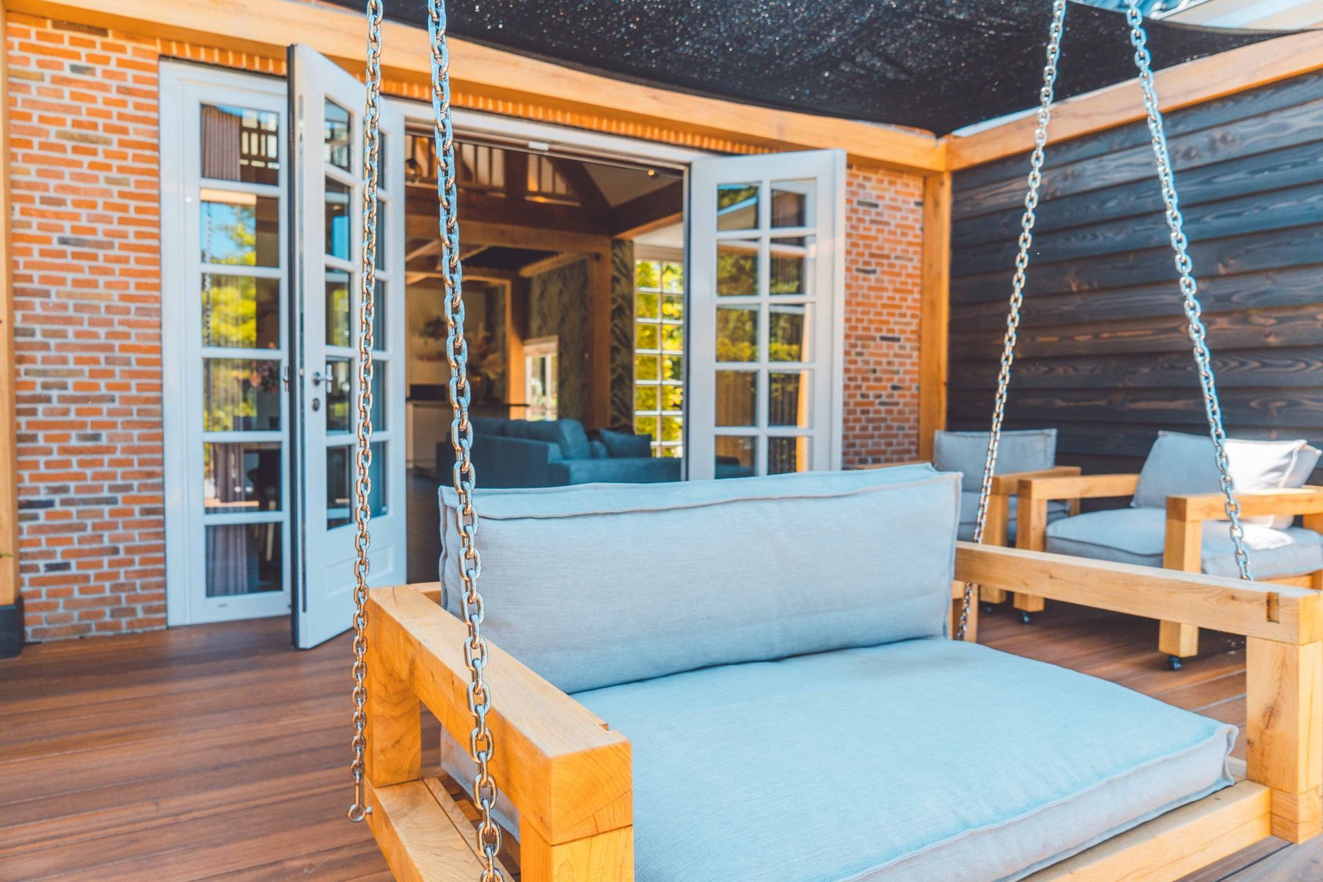 Buitenpatio met schommelbed en tuinmeubilair, openslaande deuren naar binnen.