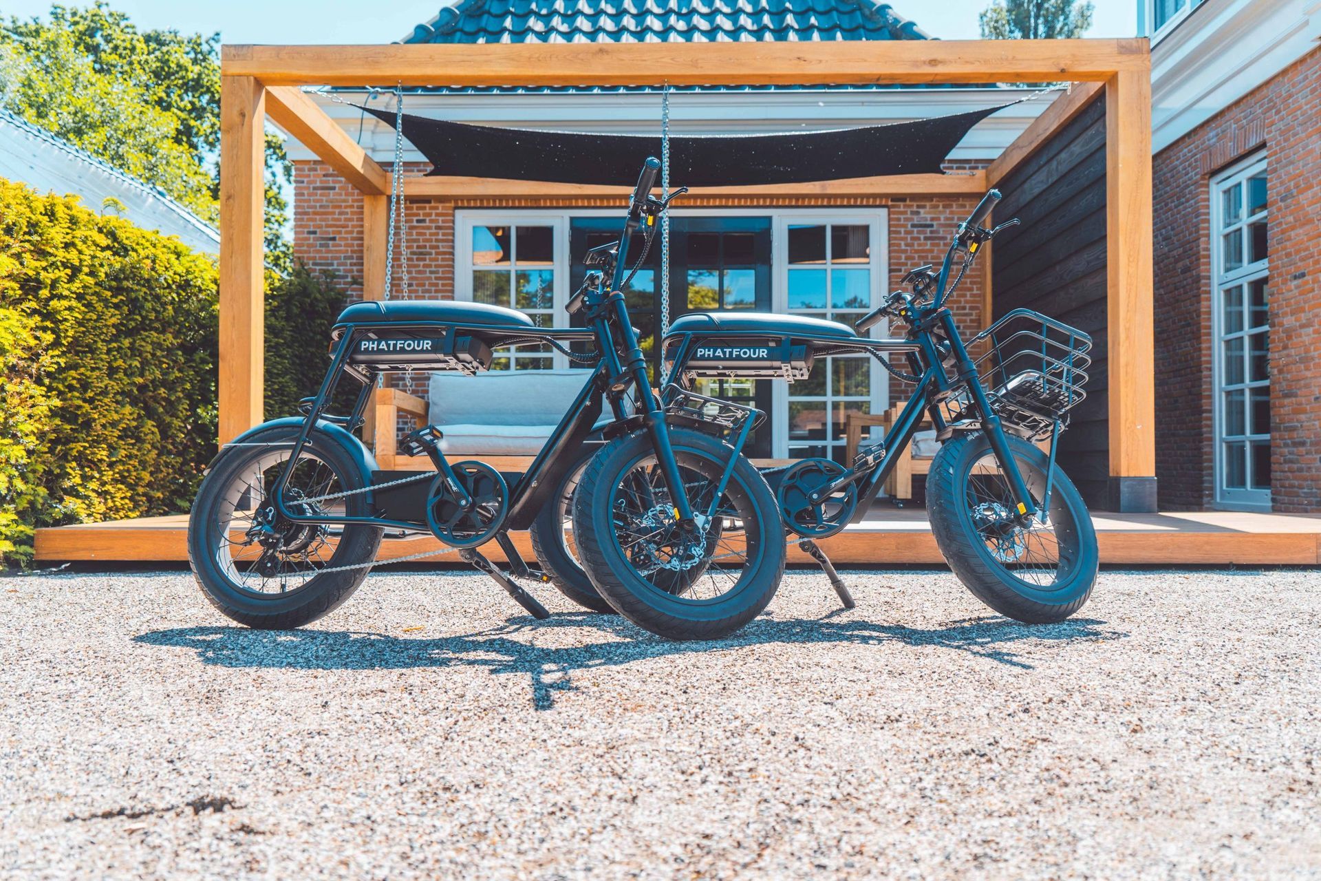 Twee zwarte elektrische fietsen staan ​​geparkeerd op het grind voor een houten constructie.