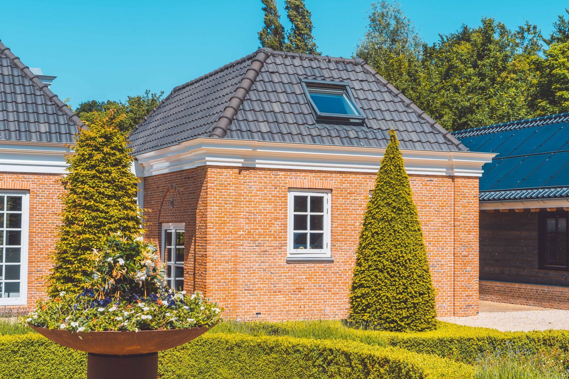 Bakstenen gebouwen met donkere pannendaken en keurig gesnoeide hagen; zonnige buitenomgeving.
