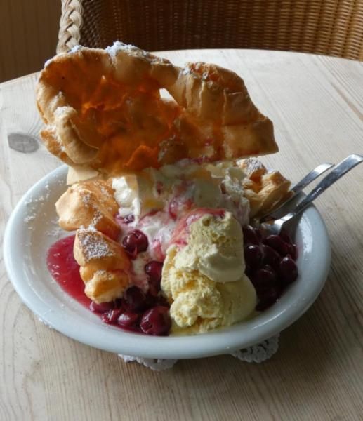 Eine Dessertschale mit Früchten, Eiscreme, Soße und einem großen Waffelplätzchen als Garnitur auf einem Tisch.