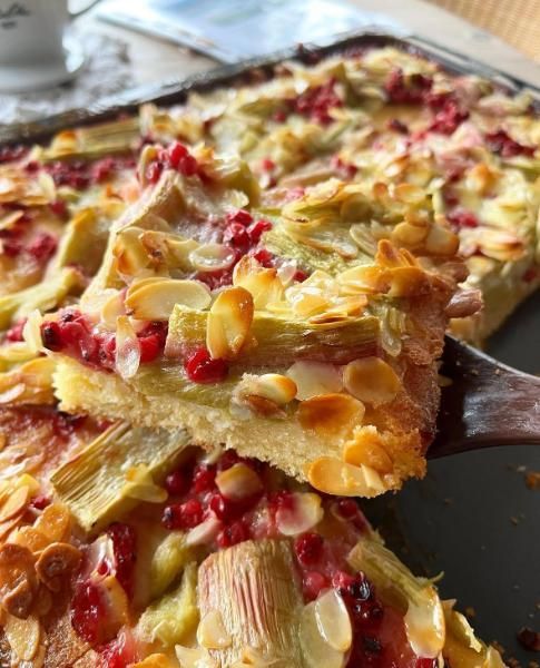 Ein Stück eines mit Früchten belegten Desserts mit roten und gelben Stücken auf einem Tablett, mit einem Spatel angehoben.
