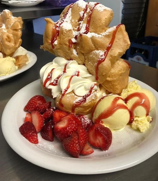 Dessertteller mit frittiertem Gebäck, Schlagsahne, Erdbeeren und rotem Sirup auf einem weißen Teller