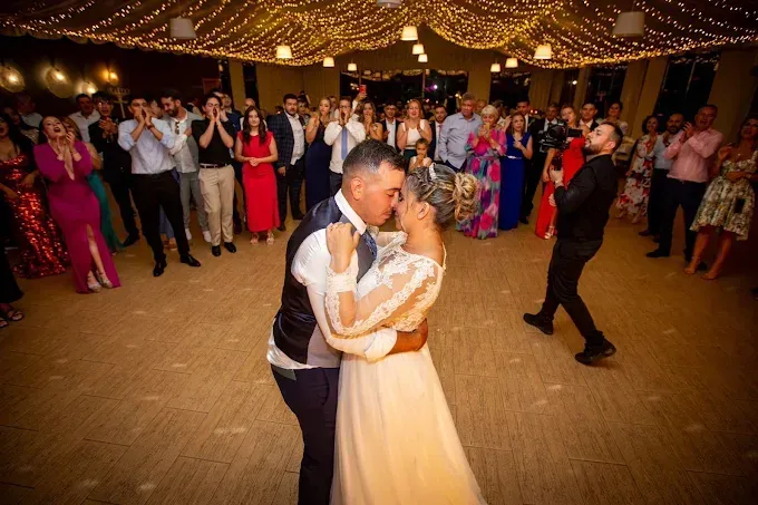 Los novios comparten un baile nupcial en el centro de un salón de baile abarrotado y decorado con guirnaldas de luces.
