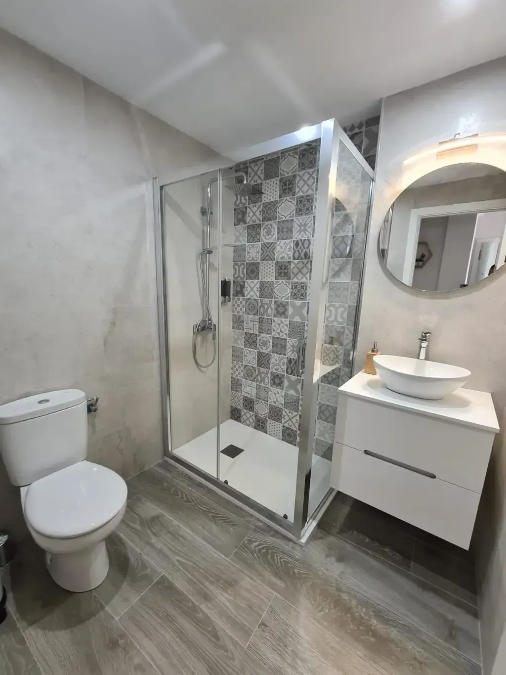 Baño moderno con ducha de cristal, inodoro y lavabo con espejo redondo.