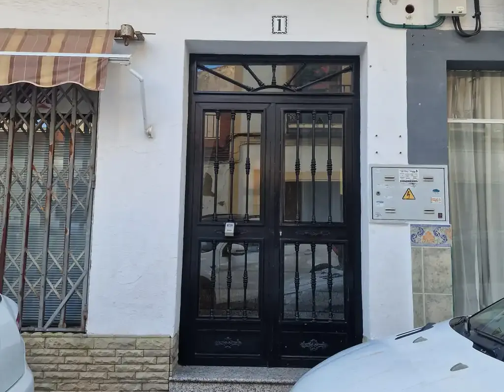 Puertas dobles negras con rejas metálicas, número "11" arriba. Toldo a la izquierda, buzones a la derecha.