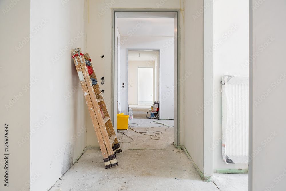 In einem im Bau befindlichen Flur lehnt eine Leiter an der Wand; durch die Türen sind andere Räume sichtbar.