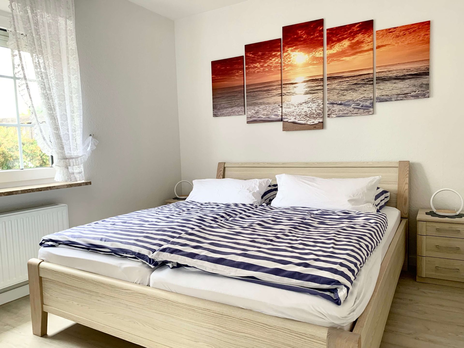 Haus Aquamarin in Büsum im Apartment Saphir - Schlafzimmer mit bezogenen Betten in einem Doppelbett 180 cm  breit - stimmungsvolles Bild im Hintergrund