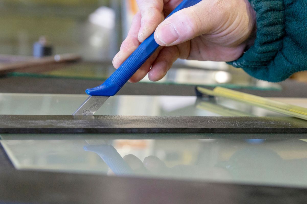 Professionnel coupant à l'aide d'un cutter bleu une fine couche de verre.