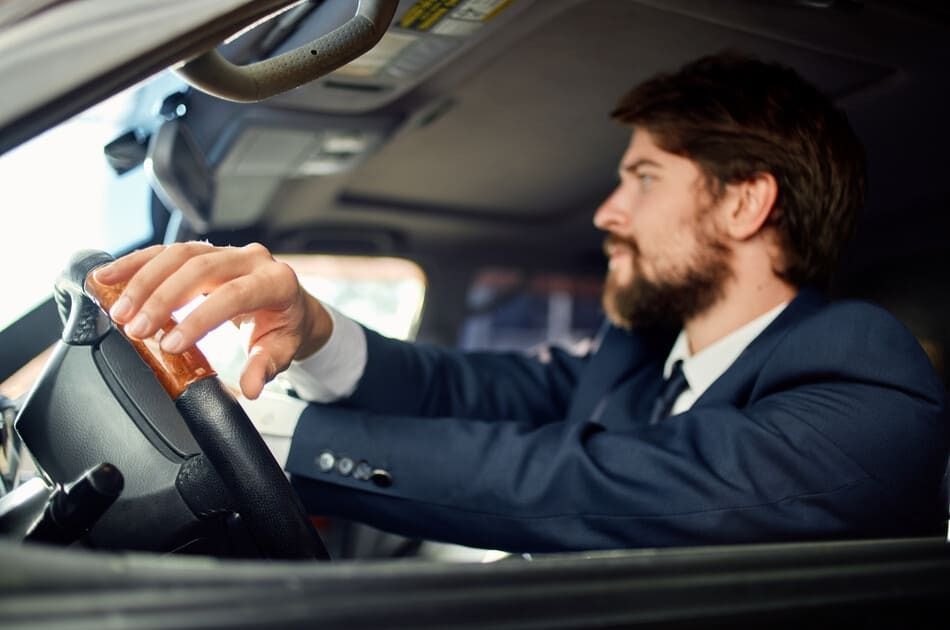 Hombre con traje azul conduciendo, con la mano apoyada en el volante.