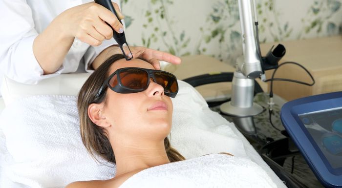 Mujer recibiendo sesiones de láser de diodo en la frente, con gafas protectoras, en un centro médico.