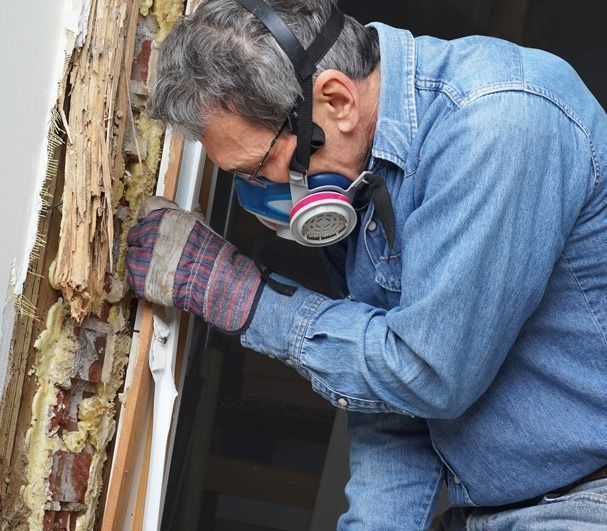 Un hombre que lleva una máscara de gas y guantes está trabajando en el marco de una ventana.