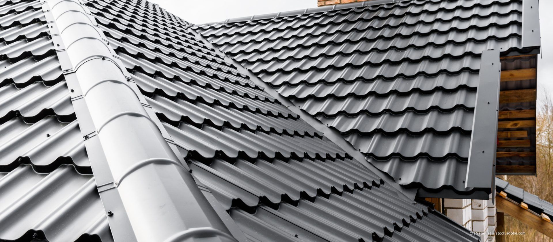 Nahaufnahme eines dunkelgrauen Metalldachziegels mit einem weißen, zylindrischen Entlüftungsrohr, das mittig verläuft.