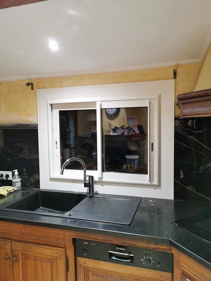 Un coin évier de cuisine avec une vasque noire, un robinet moderne et une fenêtre coulissante à cadre blanc sur une crédence foncée.