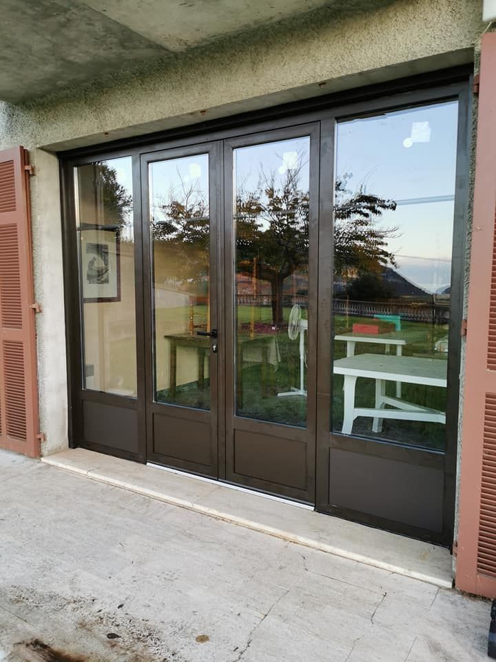 Des portes-fenêtres doubles à cadre brun s'ouvrent sur un patio où l'on aperçoit une table et des chaises.