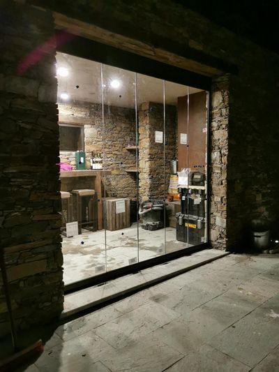 Un ensemble de portes coulissantes en verre installées dans un patio extérieur aux murs de pierre, révélant une pièce éclairée de l'intérieur.