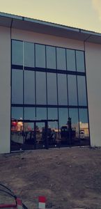 Une grande façade rectangulaire en verre foncé, intégrée au mur blanc d'un bâtiment en construction.