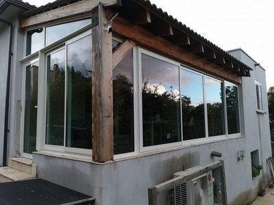 Vue extérieure d'une extension de maison caractérisée par de grandes portes coulissantes en verre et une poutre de soutien en bois proéminente.