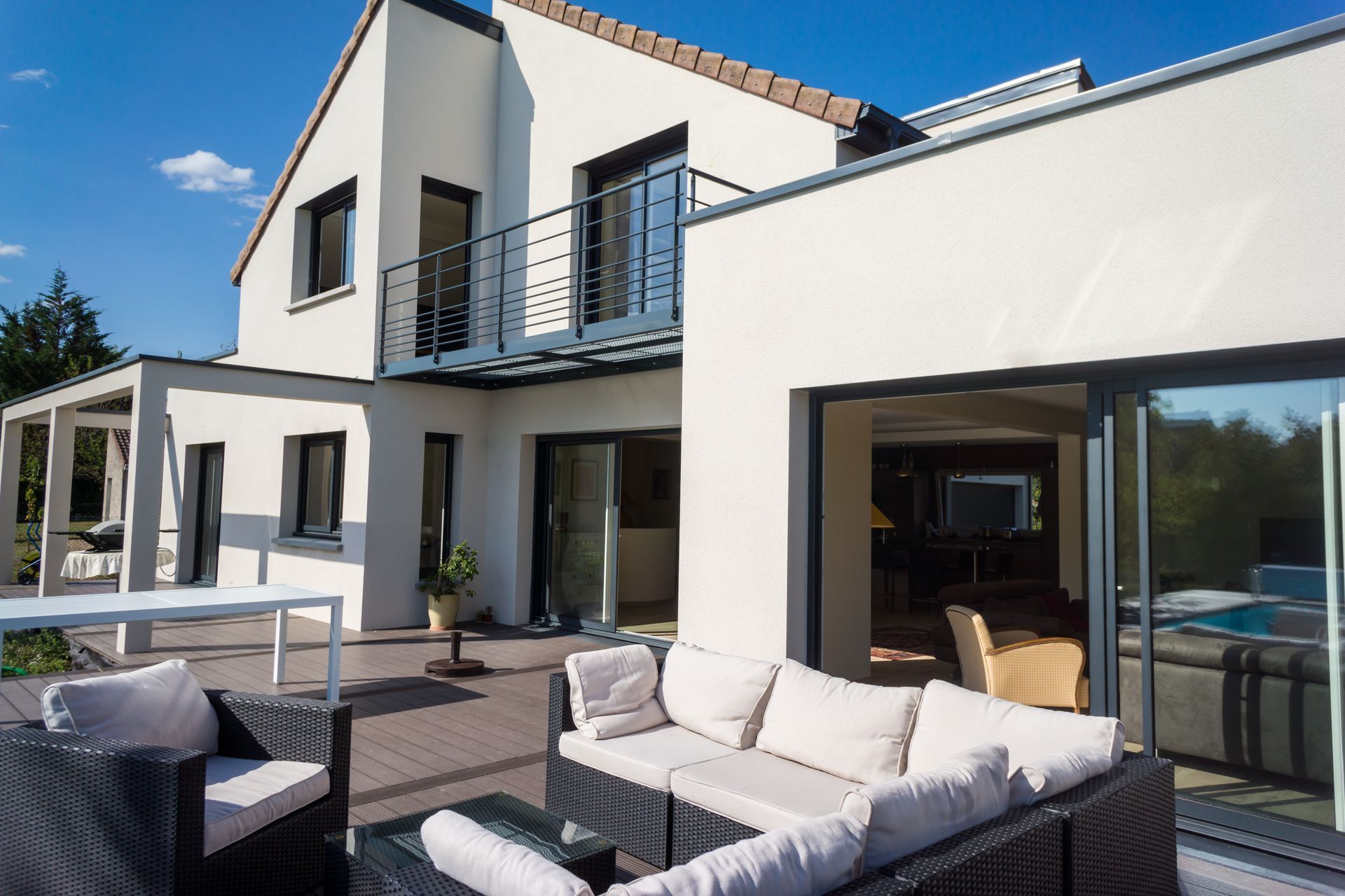 Une maison contemporaine avec une terrasse, du mobilier de jardin et un balcon par une journée ensoleillée.