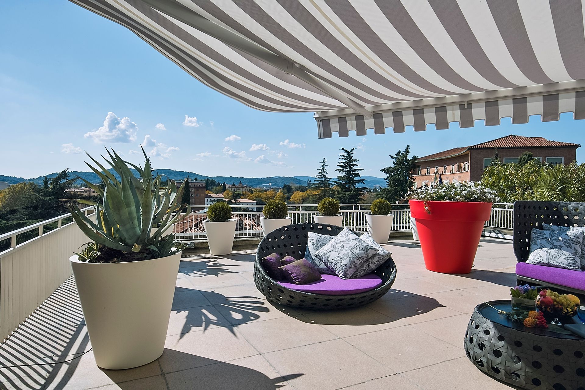 Une terrasse sur le toit moderne et ensoleillée, aménagée avec du mobilier d'extérieur, notamment un fauteuil rond, des plantes en pot et un auvent.