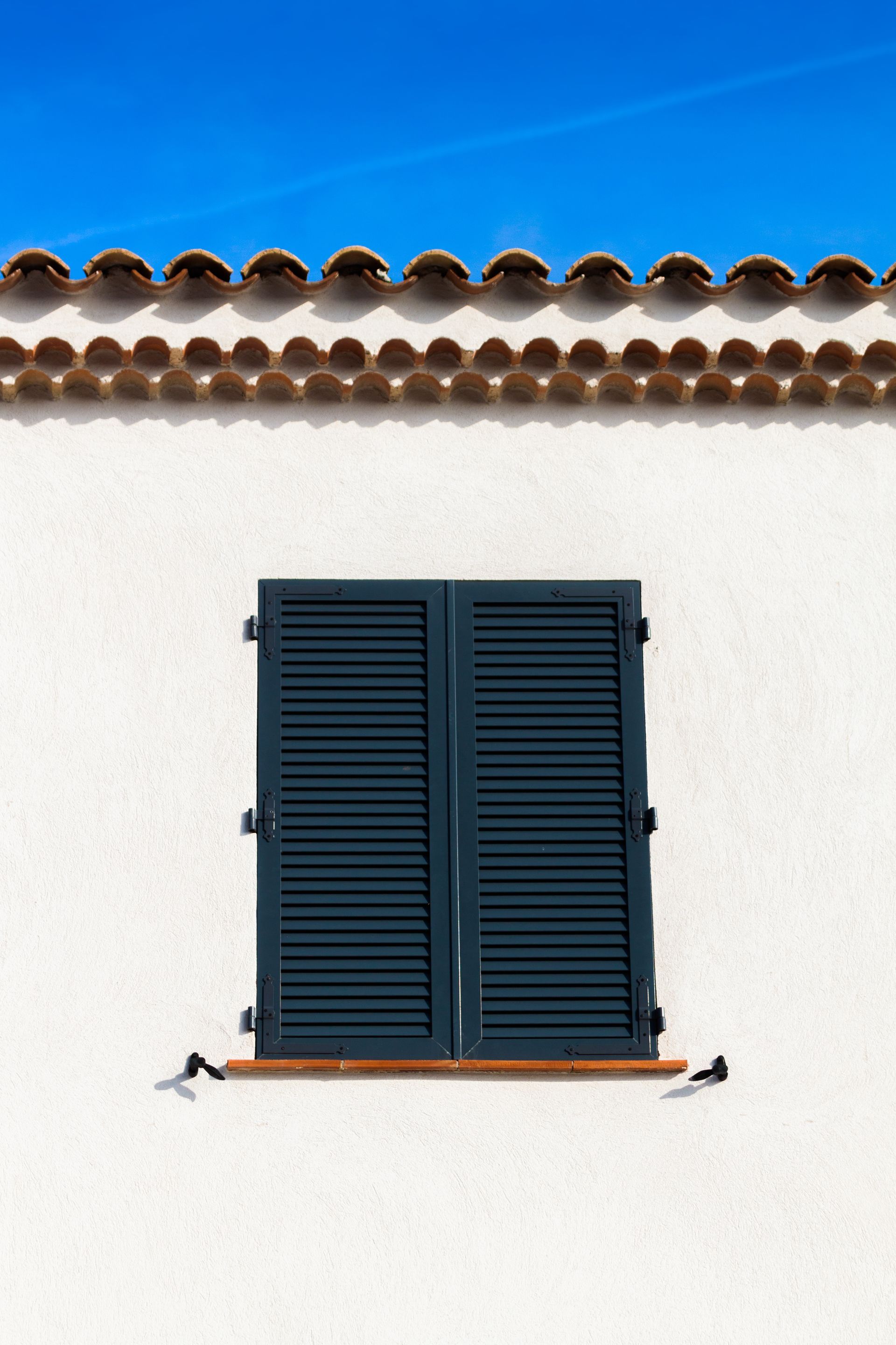 Un ensemble de portes ou de panneaux blancs à persiennes, montés sur un mur clair, laissant passer la lumière à travers les persiennes.