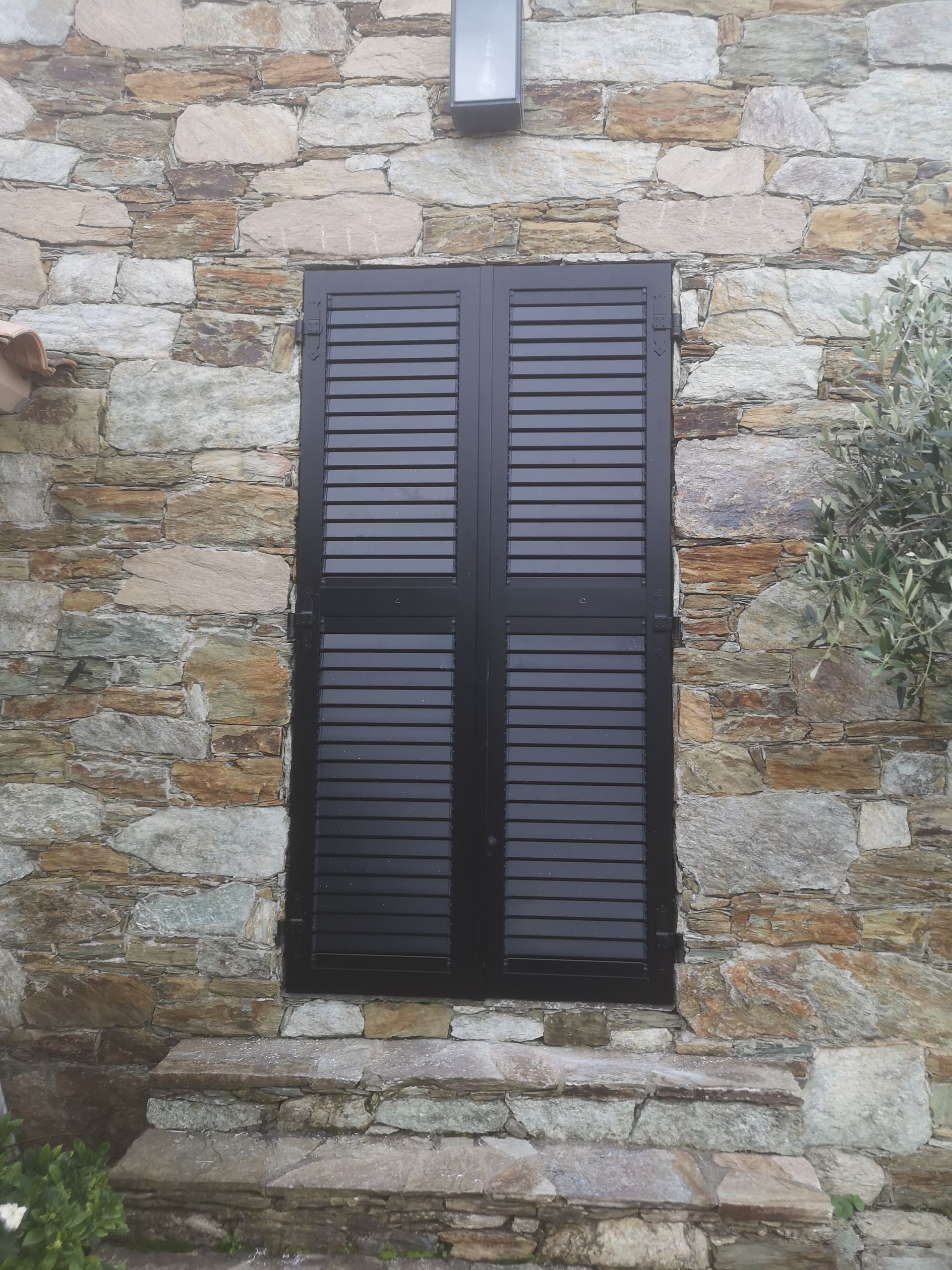 Portes à doubles volets noirs encastrées dans un mur de pierre rustique, au-dessus d'une petite marche en pierre.