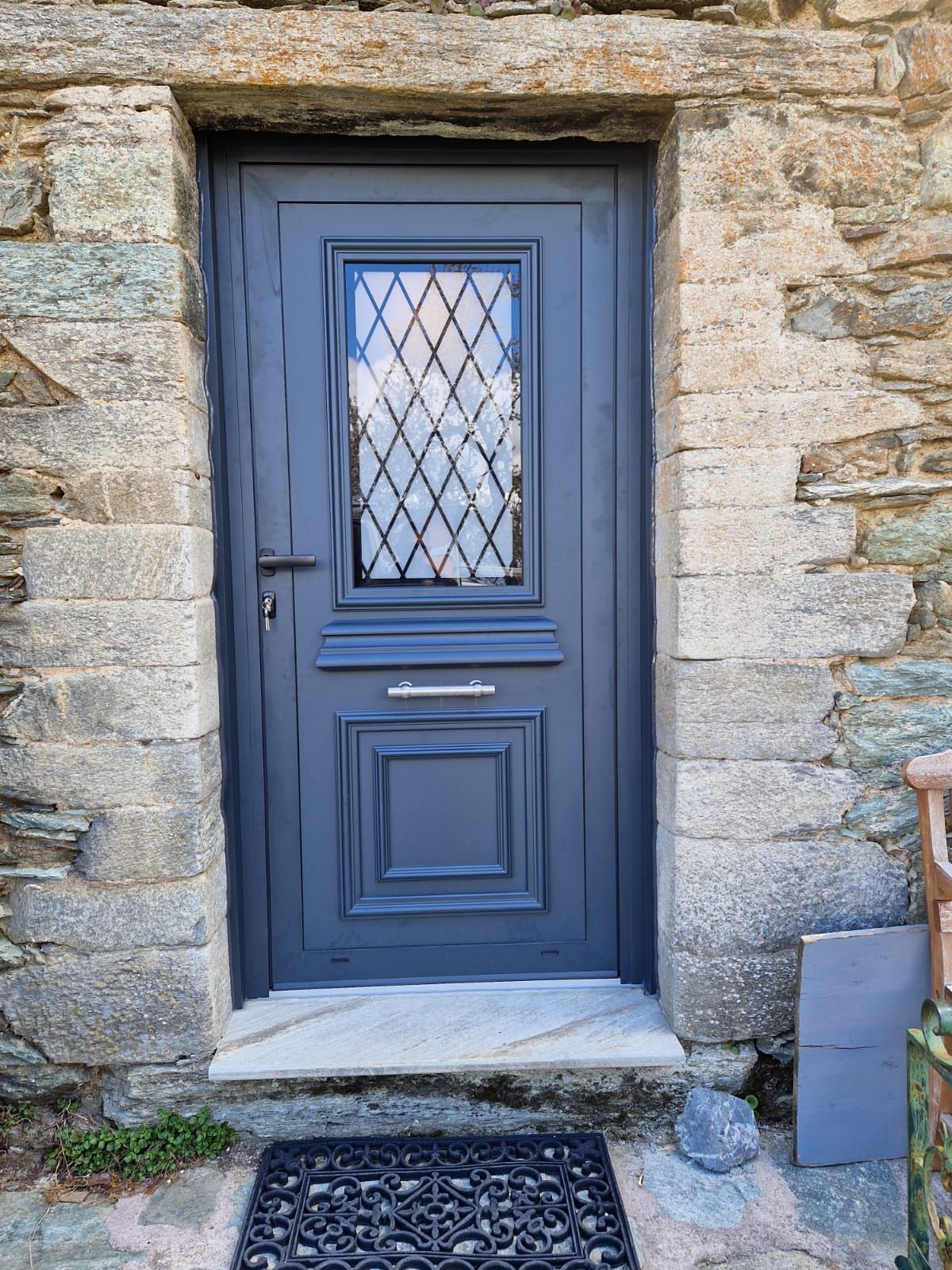 Une porte bleu foncé à un seul panneau, avec une vitre à motifs de losange, encastrée dans un encadrement de porte en pierre texturée rustique.