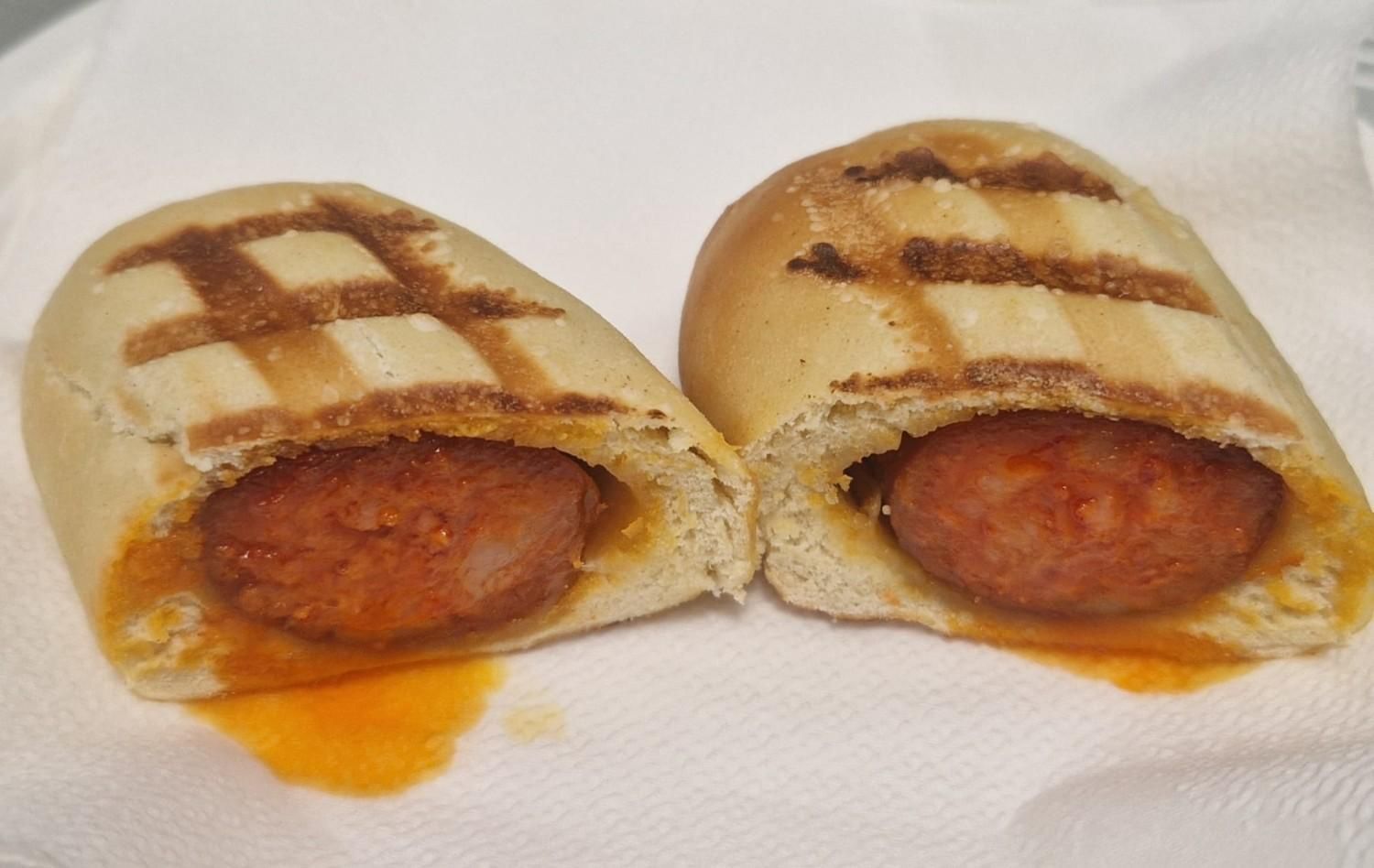 Perrito caliente con kétchup, mostaza, pepinillos y cebolla crujiente en un panecillo envuelto en papel de periódico.