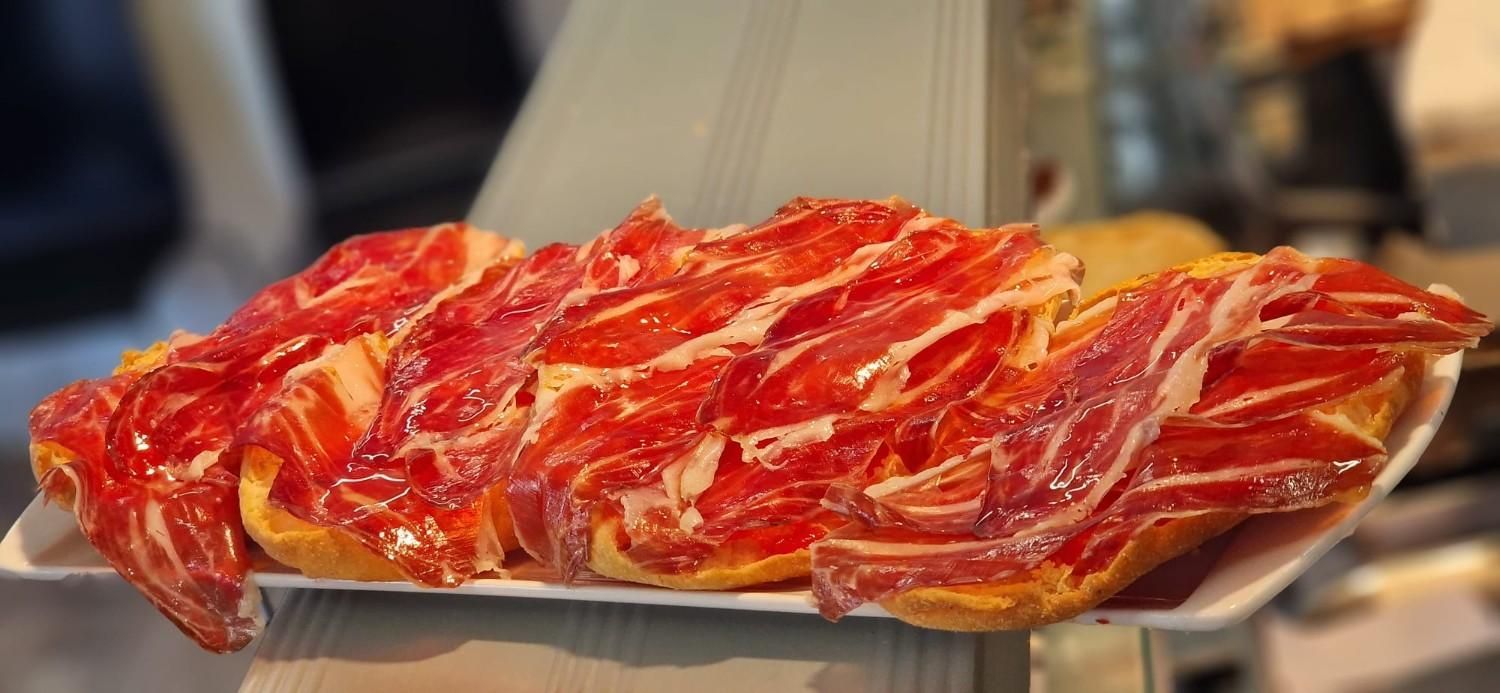 Dos rebanadas de bruschetta sobre una tabla de madera, una con tomate y la otra con prosciutto, sobre una mesa oscura.