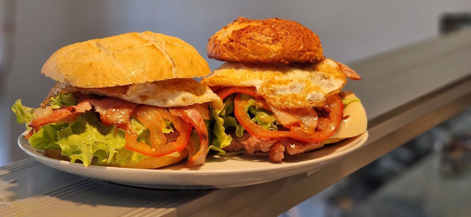 Hamburguesa con queso, lechuga, tomate y pan de sésamo, sostenida en una mano.